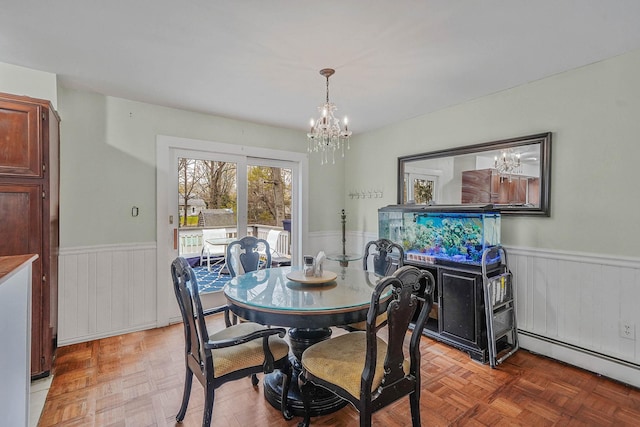 dining area featuring wainscoting, a baseboard heating unit, and a notable chandelier