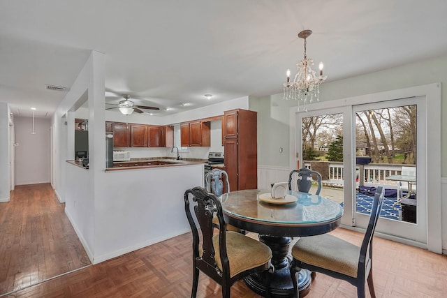 dining area featuring attic access, ceiling fan with notable chandelier, visible vents, and wainscoting