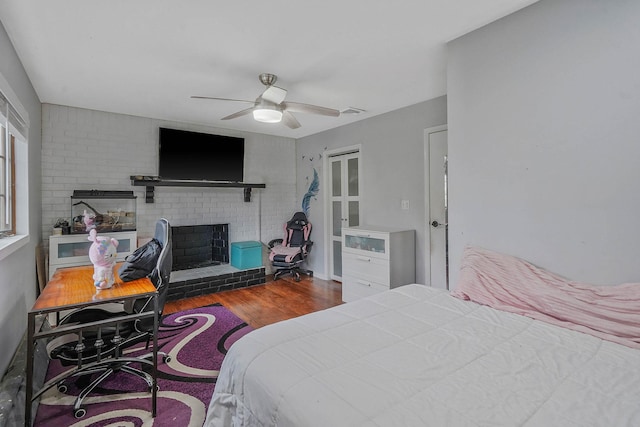 bedroom featuring wood finished floors, a brick fireplace, and ceiling fan