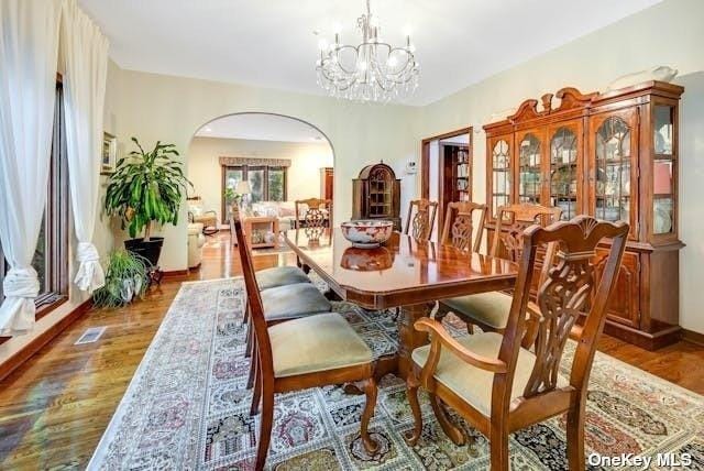 dining room featuring arched walkways, wood finished floors, an inviting chandelier, and baseboards