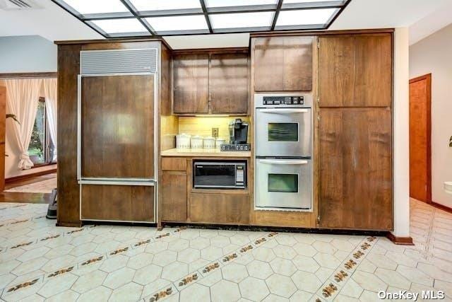 kitchen featuring built in appliances, light tile patterned floors, light countertops, visible vents, and brown cabinets