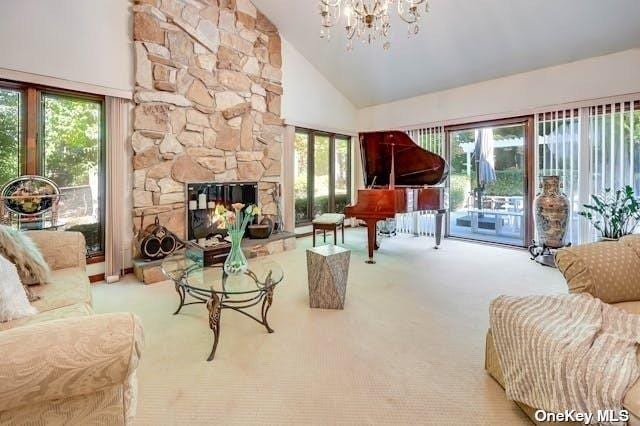 carpeted living area featuring a stone fireplace, a wealth of natural light, high vaulted ceiling, and a chandelier