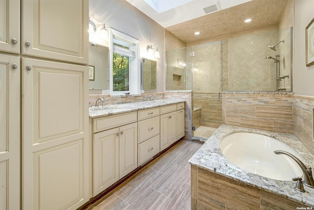 bathroom with a garden tub, visible vents, a skylight, a sink, and a stall shower