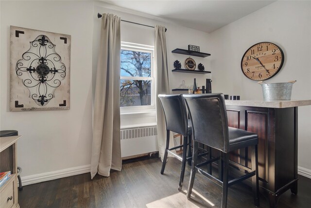 bar with a bar, baseboards, radiator, and dark wood-style floors
