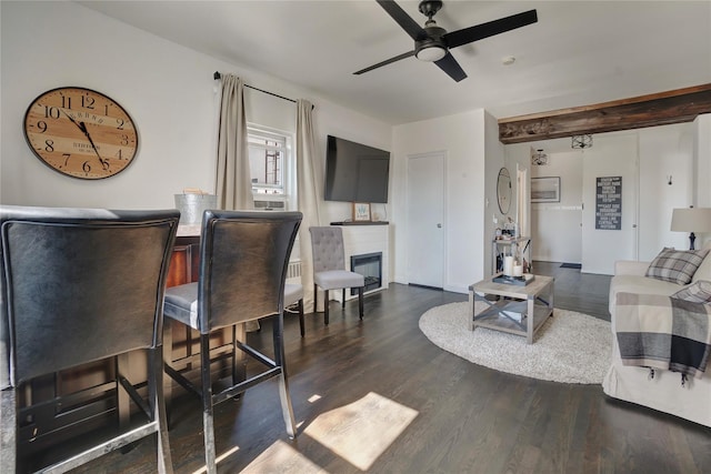 living room with dark wood-type flooring, ceiling fan, and a glass covered fireplace