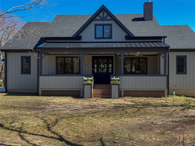 modern inspired farmhouse featuring roof with shingles, a chimney, covered porch, and a standing seam roof