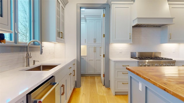 kitchen with custom exhaust hood, dishwasher, a sink, stove, and decorative backsplash