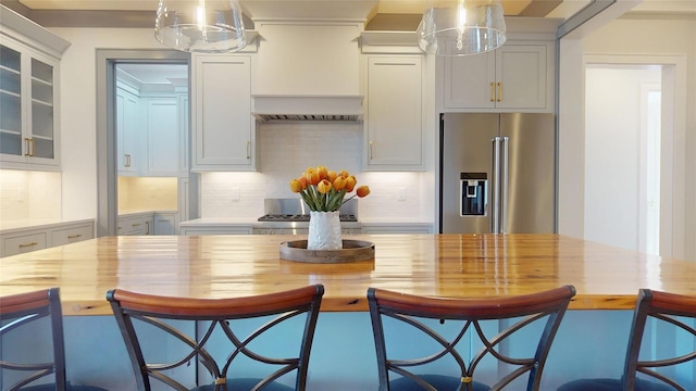 kitchen with butcher block countertops, glass insert cabinets, backsplash, high end refrigerator, and hanging light fixtures