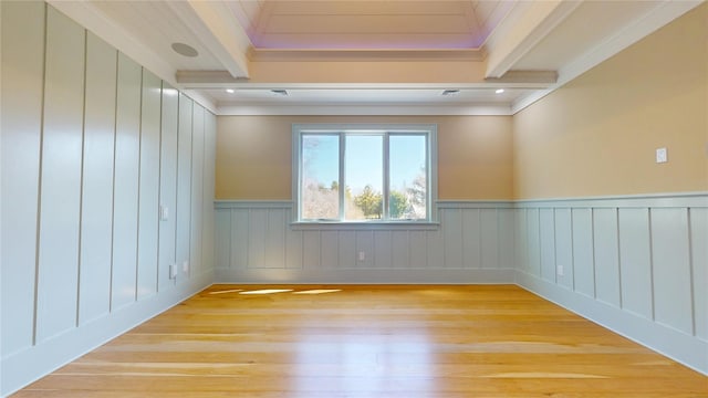 spare room with crown molding, beamed ceiling, a wainscoted wall, and light wood finished floors