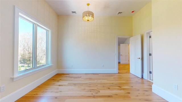 unfurnished room featuring light wood-type flooring, an inviting chandelier, baseboards, and visible vents