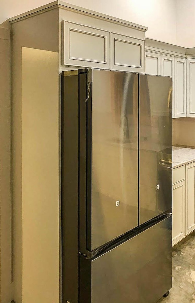 interior space with light stone counters, white cabinets, freestanding refrigerator, and concrete flooring