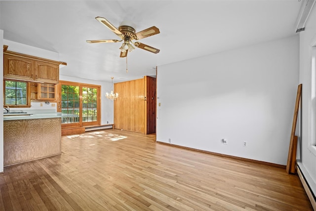 unfurnished living room with baseboards, baseboard heating, ceiling fan with notable chandelier, light wood-style flooring, and a baseboard heating unit