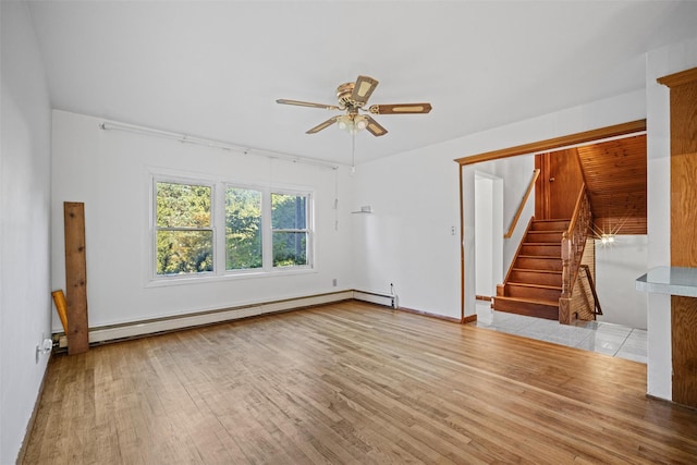 unfurnished living room featuring stairs, baseboard heating, a ceiling fan, and wood finished floors