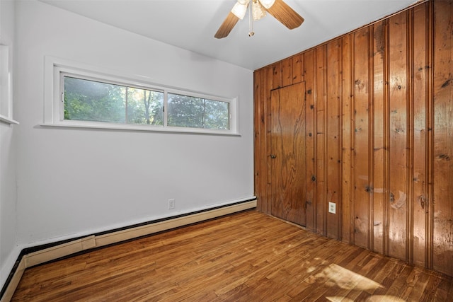 unfurnished room featuring a baseboard radiator, wood finished floors, wood walls, and a ceiling fan
