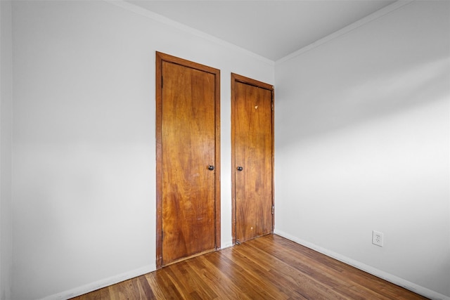 unfurnished bedroom featuring crown molding, baseboards, two closets, and wood finished floors