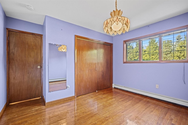 unfurnished bedroom with baseboard heating, a closet, and wood finished floors
