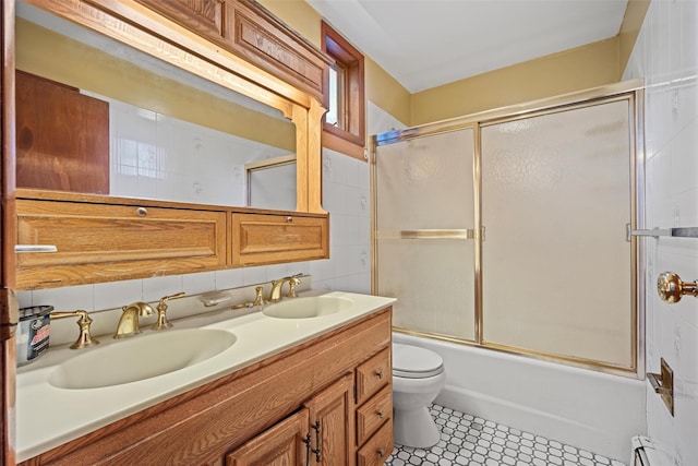 full bath featuring toilet, shower / bath combination with glass door, double vanity, and a sink