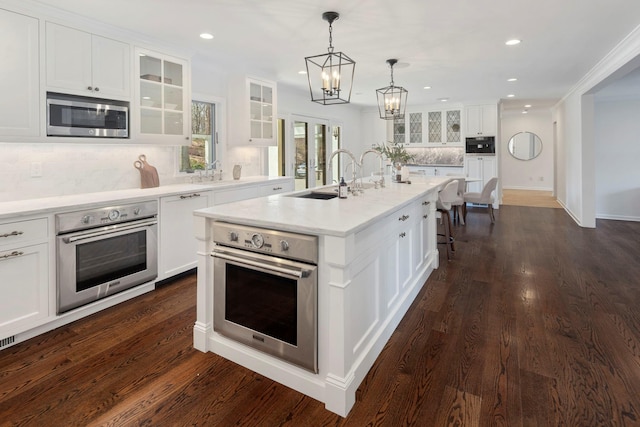 kitchen featuring a sink, stainless steel appliances, a notable chandelier, white cabinets, and backsplash