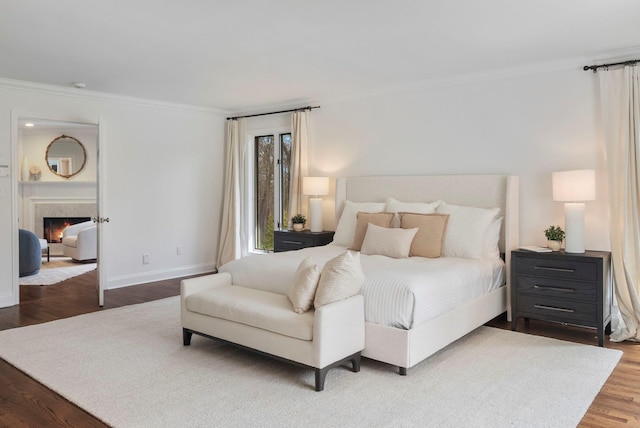 bedroom featuring crown molding, a lit fireplace, wood finished floors, and baseboards