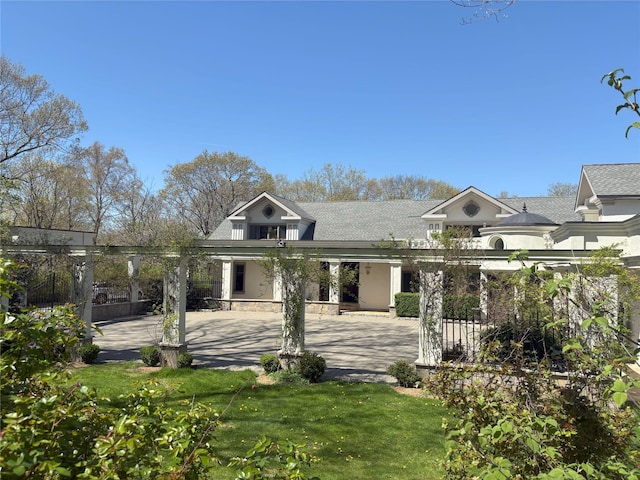 view of front of house featuring a front lawn, a patio area, roof with shingles, and fence
