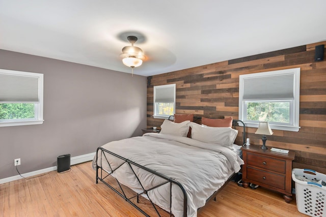 bedroom featuring wooden walls, baseboards, an accent wall, and light wood-style flooring