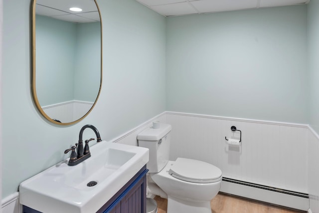 bathroom featuring a baseboard heating unit, a wainscoted wall, toilet, wood finished floors, and vanity