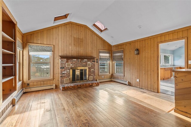 46 Mount Grey Rd, Setauket, NY 11733 - unfurnished living room featuring a skylight, light wood finished floors, lofted ceiling, wooden walls, and baseboard heating