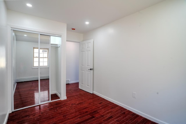 unfurnished bedroom featuring a closet, a baseboard heating unit, baseboards, recessed lighting, and wood finished floors