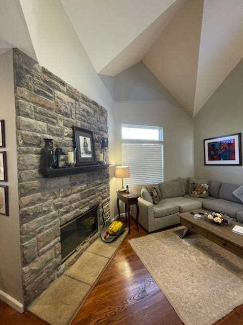 living room featuring a stone fireplace, wood finished floors, and lofted ceiling