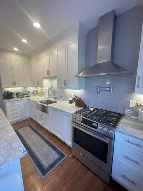 kitchen with a sink, white cabinets, dark wood finished floors, wall chimney exhaust hood, and stainless steel gas range oven