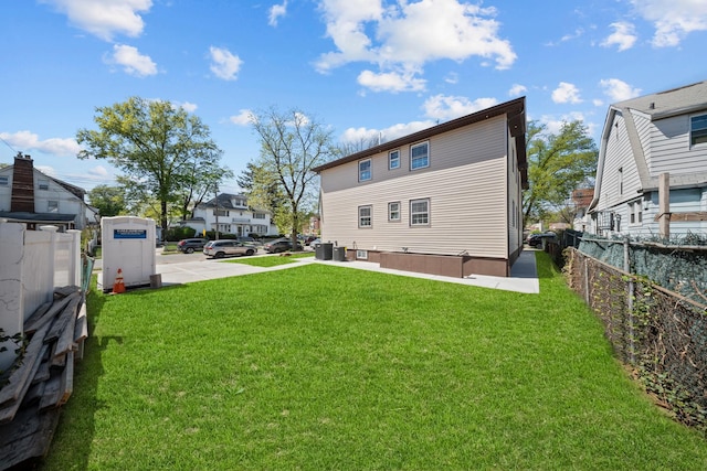 back of property featuring a lawn, central AC, fence, and a residential view