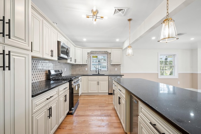 kitchen with appliances with stainless steel finishes, a sink, light wood-style floors, decorative light fixtures, and visible vents