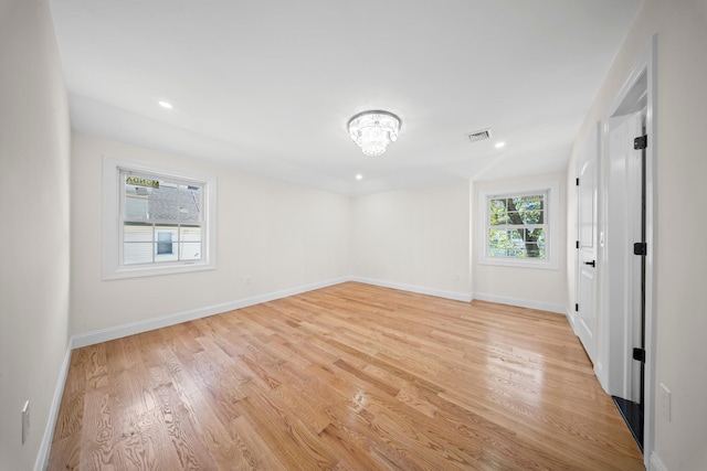 unfurnished room with visible vents, light wood finished floors, baseboards, and a chandelier