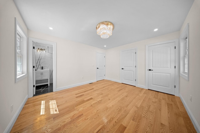 unfurnished bedroom with baseboards, light wood-style flooring, ensuite bathroom, and a notable chandelier