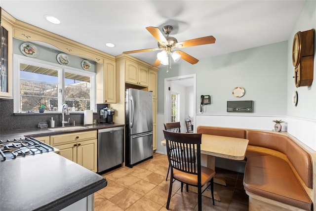 kitchen with dark countertops, a sink, cream cabinetry, and appliances with stainless steel finishes
