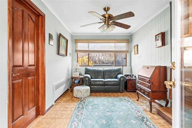 living area with radiator, wooden walls, a ceiling fan, ornamental molding, and baseboards