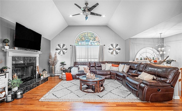 living area featuring ceiling fan with notable chandelier, vaulted ceiling, wood finished floors, and a fireplace