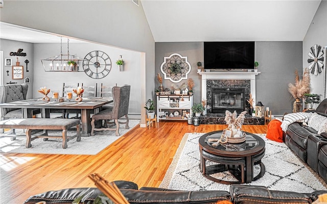 living room featuring vaulted ceiling, wood finished floors, a high end fireplace, an inviting chandelier, and baseboards
