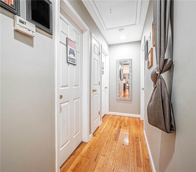 hallway featuring light wood-type flooring, attic access, and baseboards