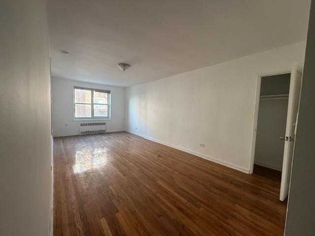 34-15 74th St Unit 4H, Jackson Heights, NY 11372 - spare room with radiator, wood finished floors, and baseboards