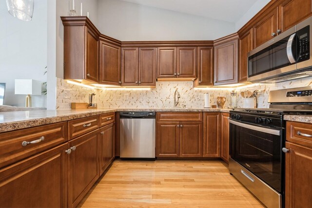 kitchen with decorative backsplash, vaulted ceiling, appliances with stainless steel finishes, and light wood-style floors