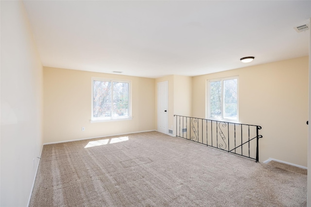 carpeted spare room featuring baseboards, visible vents, and plenty of natural light