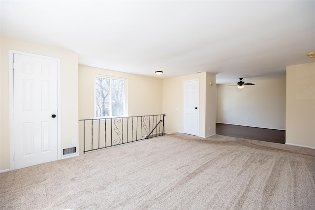 empty room with visible vents, carpet flooring, baseboards, and a ceiling fan