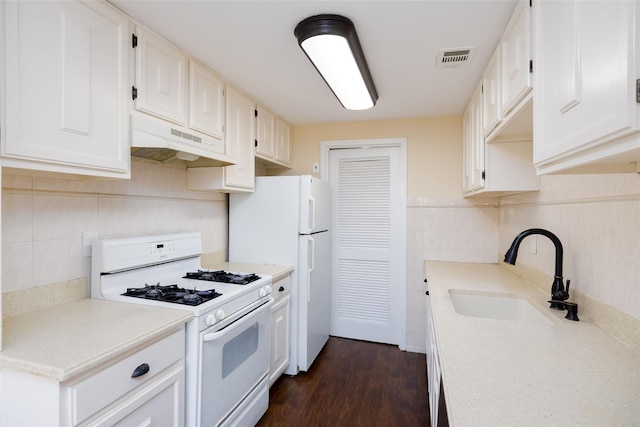 kitchen featuring under cabinet range hood, backsplash, a sink, white appliances, and tile walls
