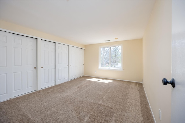 unfurnished bedroom featuring multiple closets, carpet flooring, baseboards, and visible vents