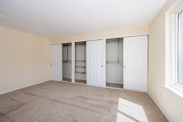 unfurnished bedroom featuring baseboards, carpet floors, and two closets