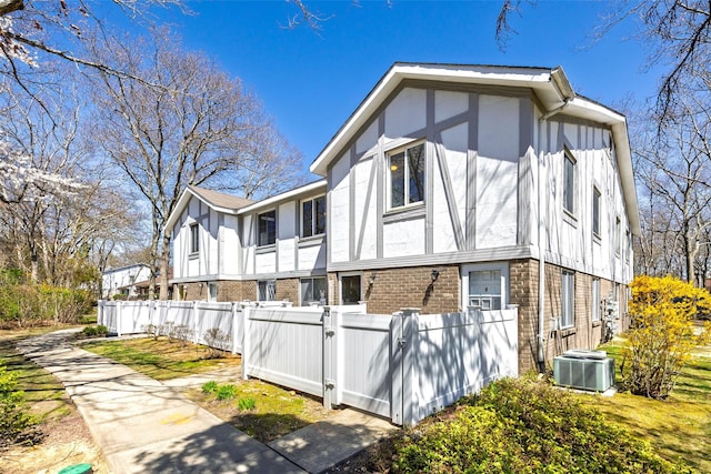 view of property exterior with a gate, fence private yard, brick siding, and central AC unit