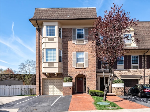 townhome / multi-family property with brick siding, fence, a shingled roof, and a garage
