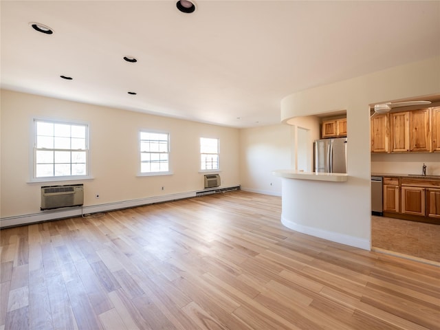 unfurnished living room featuring an AC wall unit, a sink, and light wood-style flooring