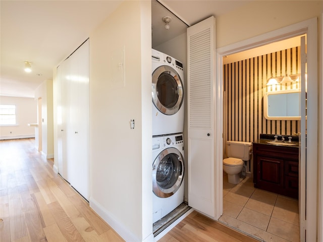 washroom featuring stacked washer and dryer, laundry area, baseboard heating, a sink, and light wood-type flooring